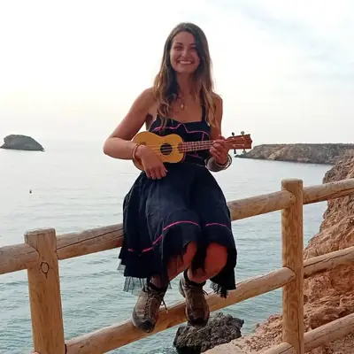 Leyla spielt Ukulele auf einem Holzgeländer am Meer