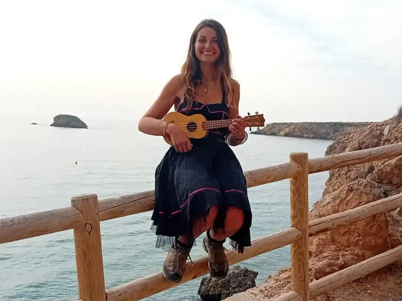 Leyla spielt Ukulele auf einem Holzgeländer über dem Meer